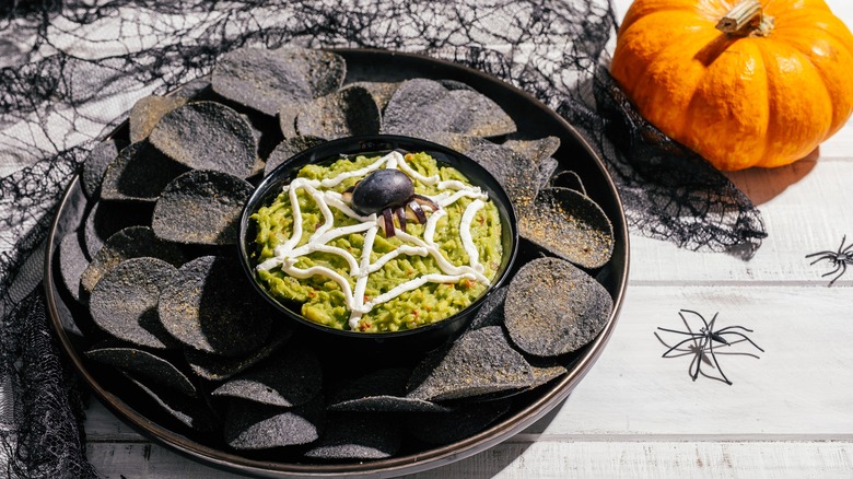 A bowl of spider web guacamole with chips and an olive spider