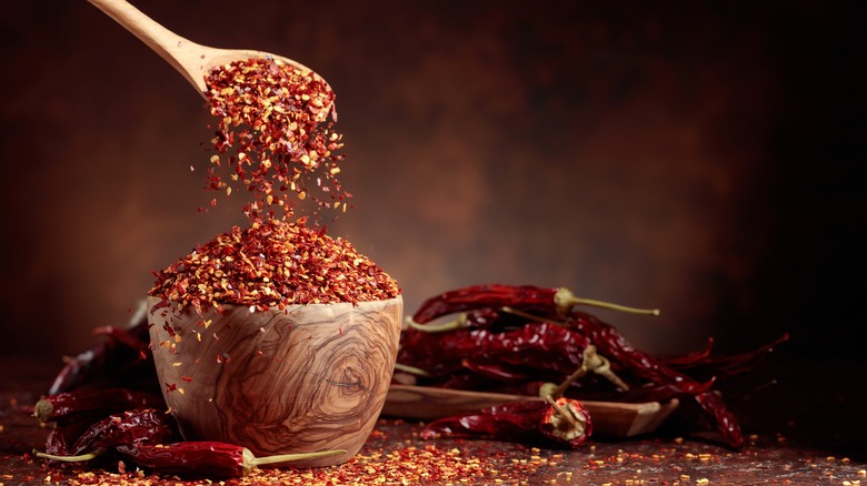 A wooden spoon scoops red pepper flakes out of bowl