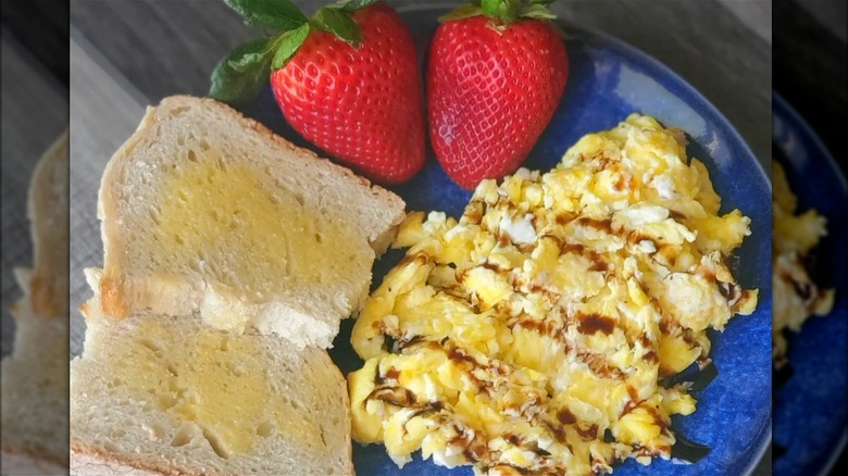 Scrambled eggs with vinegar and toast with strawberries on blue plate