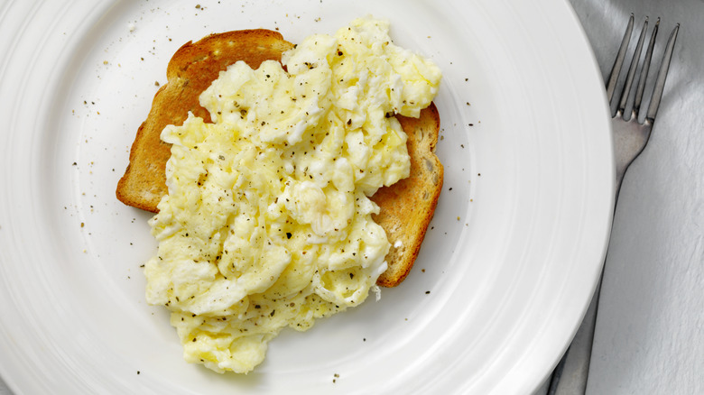 Scrambled eggs over toast on plate with fork