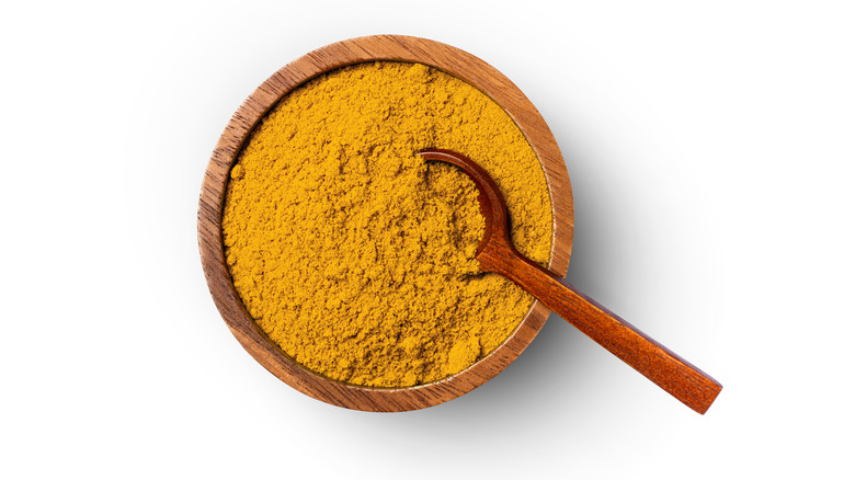 Curry powder with spoon on white background