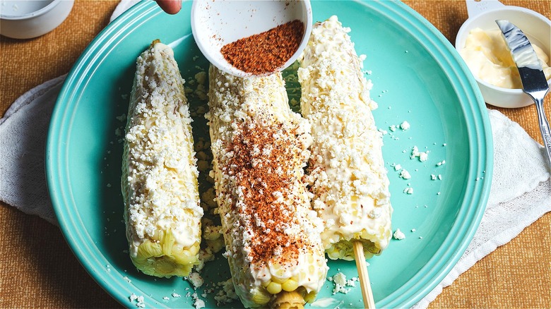 Hand adding spices to Mexican corn 