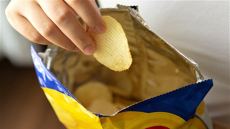 Potato chip in hand over bag