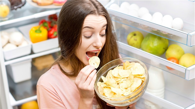 Woman eating chips out of refrigerator