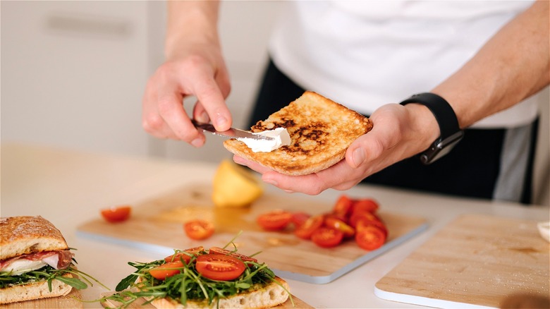 Hand spreading cream cheese on bread