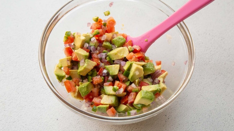 salsa made with avocado and tomatoes in a glass bowl with a pink spoon