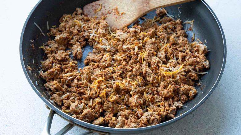 ground meat and cheese in frying pan with wooden spatula