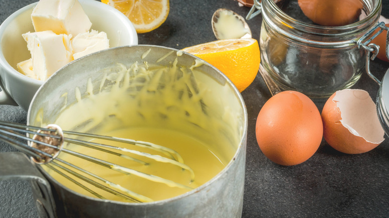 whisk in a pot of hollandaise next to ingredients