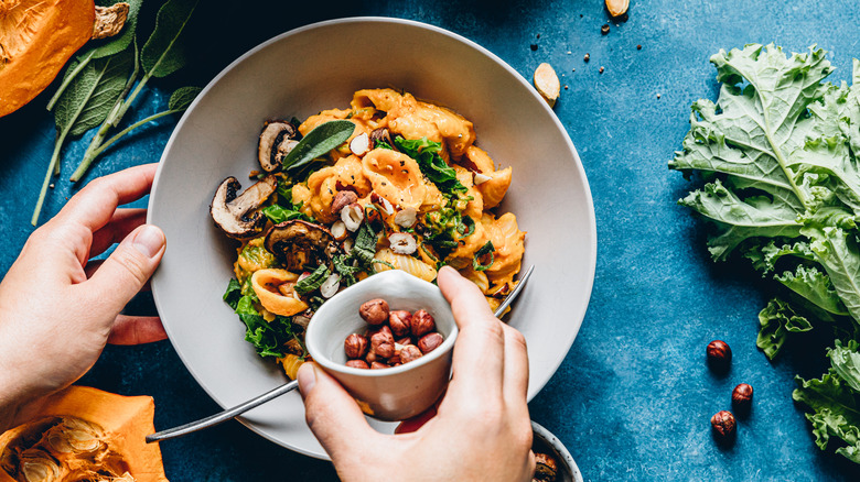 Person adding hazelnuts to vegetable pasta dish