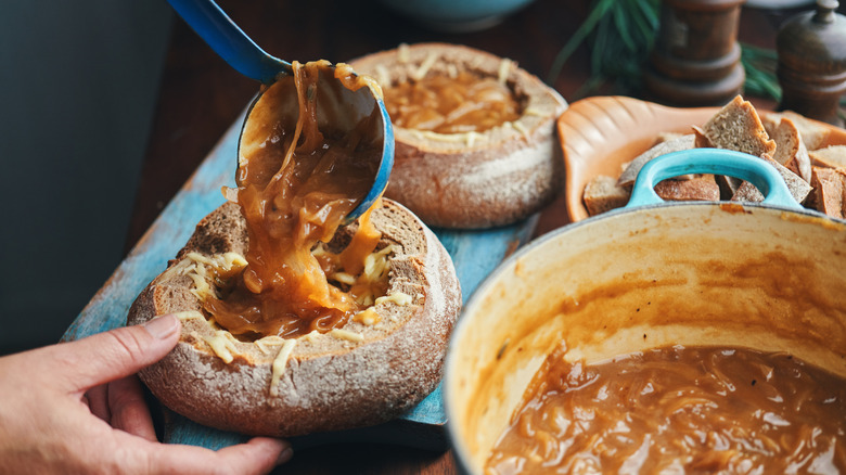 Ladle spooning French onion soup into bread bowls