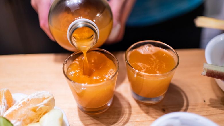 Hands pour orange kombucha into two cups