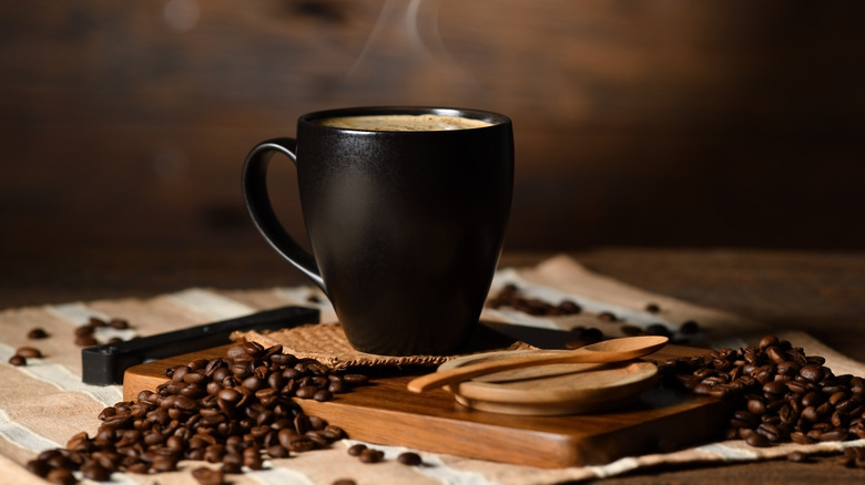 Steaming mug beside coffee beans