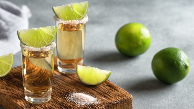 Two shots of tequila on a wooden board with salt and limes