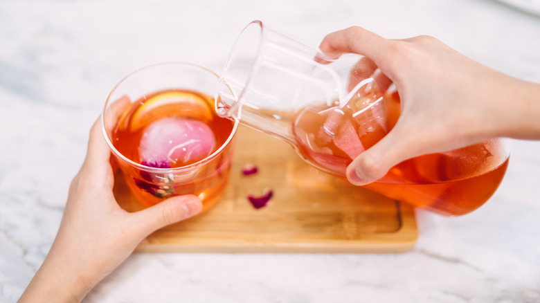 hands pouring iced tea from jug to glass