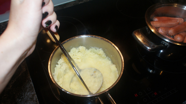 Person stirring mashed potatoes in pot