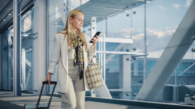 Woman walking in an airport looking at phone and smiling