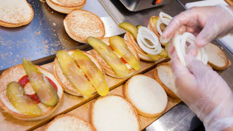 gloved hands putting ingredients on buns