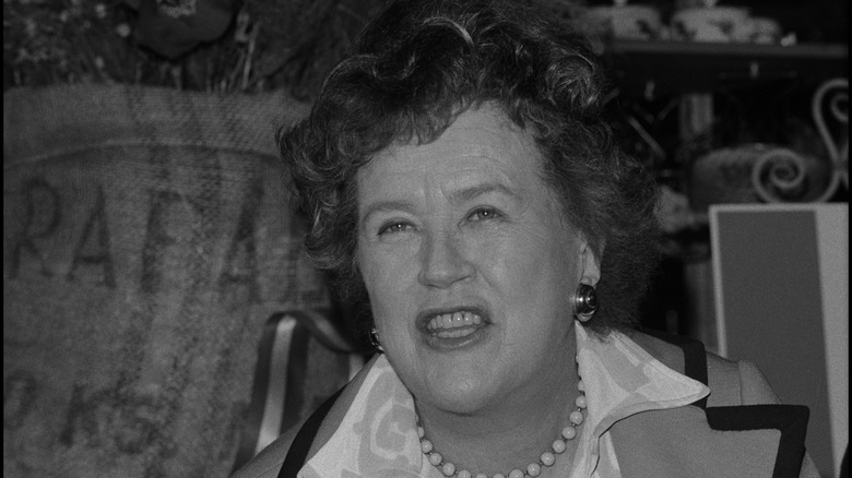 Julia Child smiles behind a plate of food