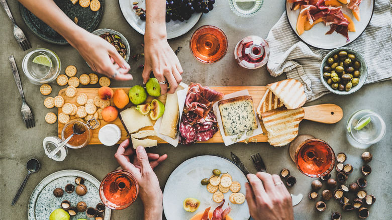 Two people reaching for snacks from a charcuterie board paired with wine