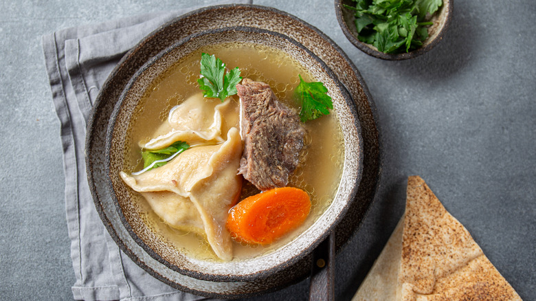 Kreplach floating in chicken soup in gray bowl against gray background