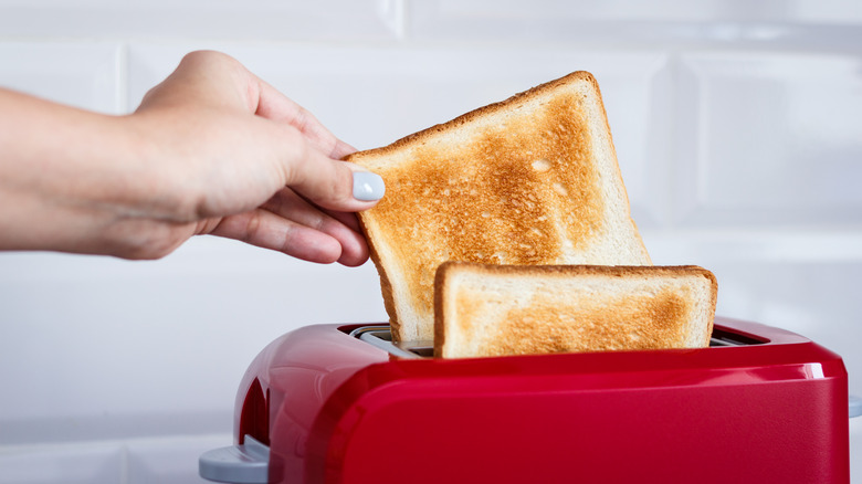 Person pulling slice of toast from red toaster