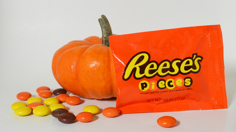 Reese's pieces next to a mini pumpkin against a white background