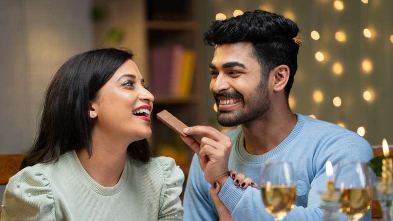 attractive couple on a date eating milk chocolate and drinking wine