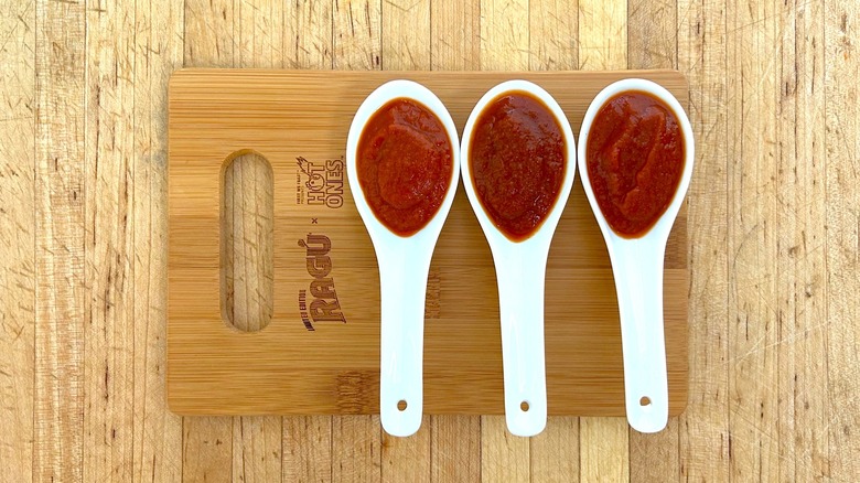 Spoonful of three RAGÚ x Hot Ones sauces on wooden cutting board