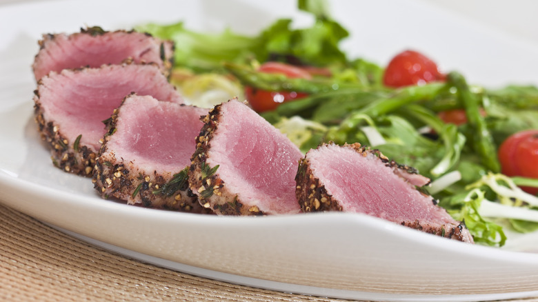 Sliced seared crusted tuna with a side salad on a plate