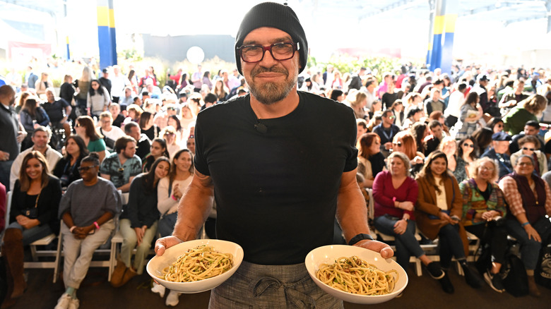 Chef Michael Symon holding bowls of pasta in front of crowd