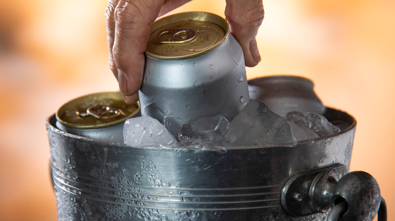 Person picking up beer can from ice bucket