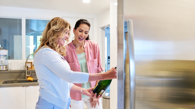 women looking at champagne bottle from the fridge