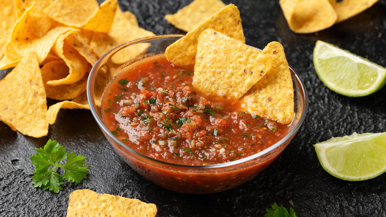 A bowl of salsa with chips and limes