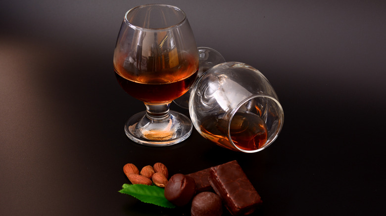 Two glasses of bourbon, one tipped, with nuts, chocolate and mint leaves