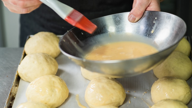 Person applying egg wash to dough