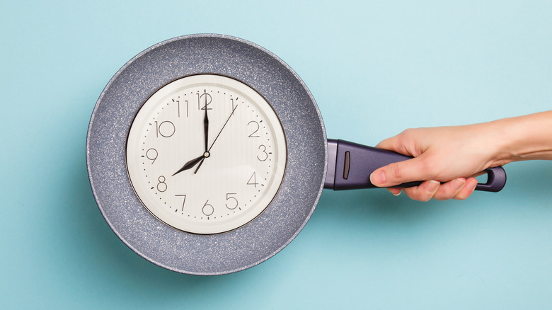 Person holding skillet with clock inside