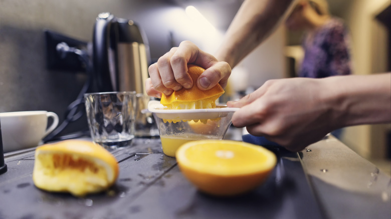 hands squeezing orange with juicer