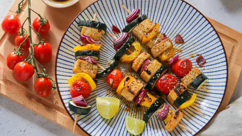 Grilled tofu skewers on a plate with cherry tomatoes and lime