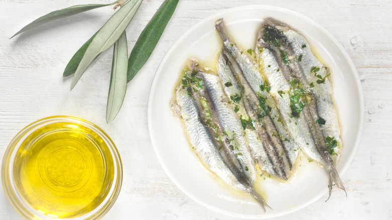 Sardine fillets on a white plate with a bowl of oil