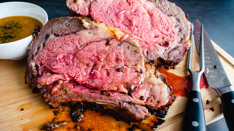 Thick slices of rare prime rib roast on a cutting board with a knife and carving fork