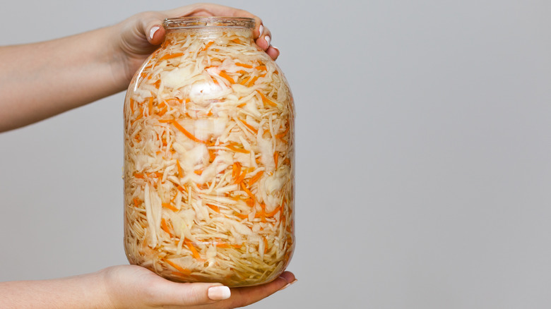 Sauerkraut in a large glass jar held by two hands