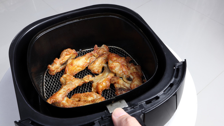 Person holding an air fryer basket with chicken wings in it