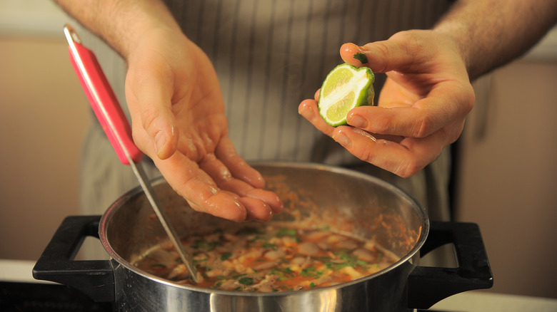 A man holds a lime in front of a pot of soup