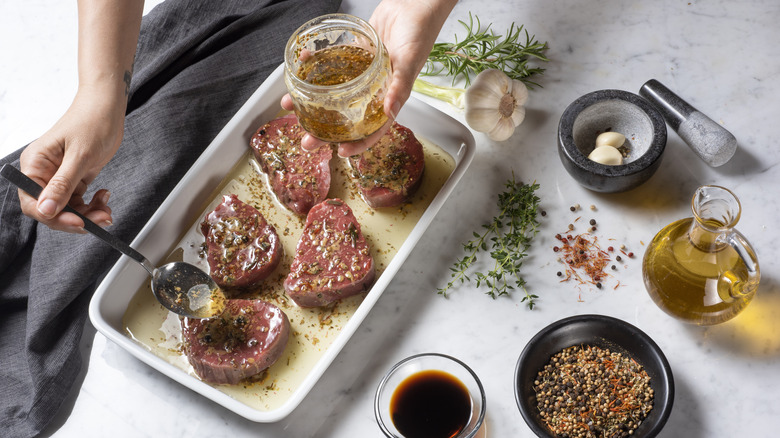 Person marinading meat in pan; ingredients on the side