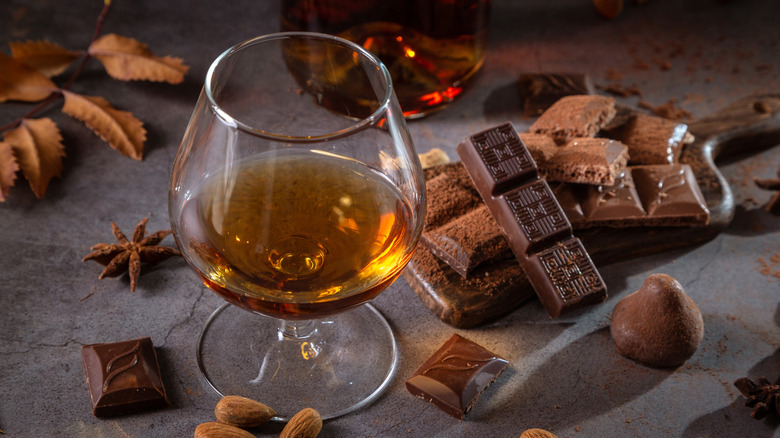 glass of Cognac surrounded by chocolate and nuts on a dark background