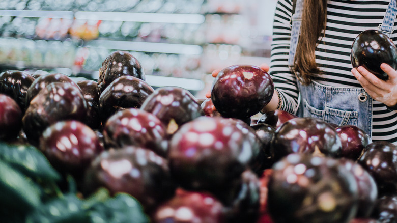 Person choosing eggplant at grocery store