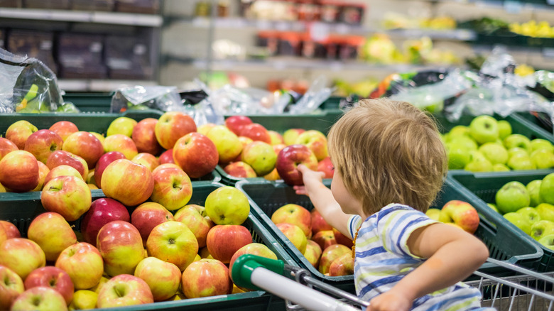 child picking apple in grocery store