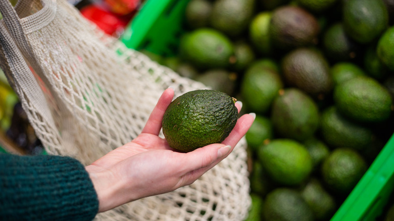 woman choosing avocado at market