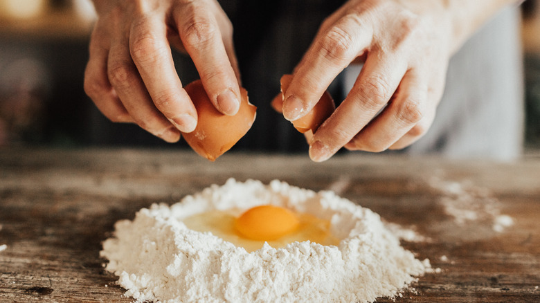 hands cracking egg over pile of flour 