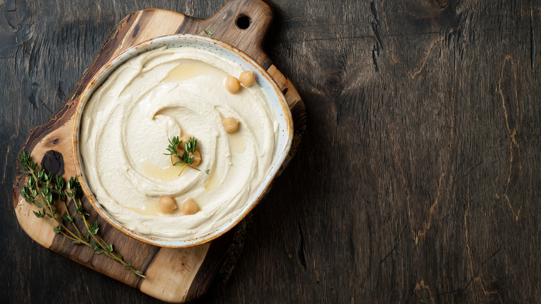 Big bowl of hummus on wooden cutting board with thyme